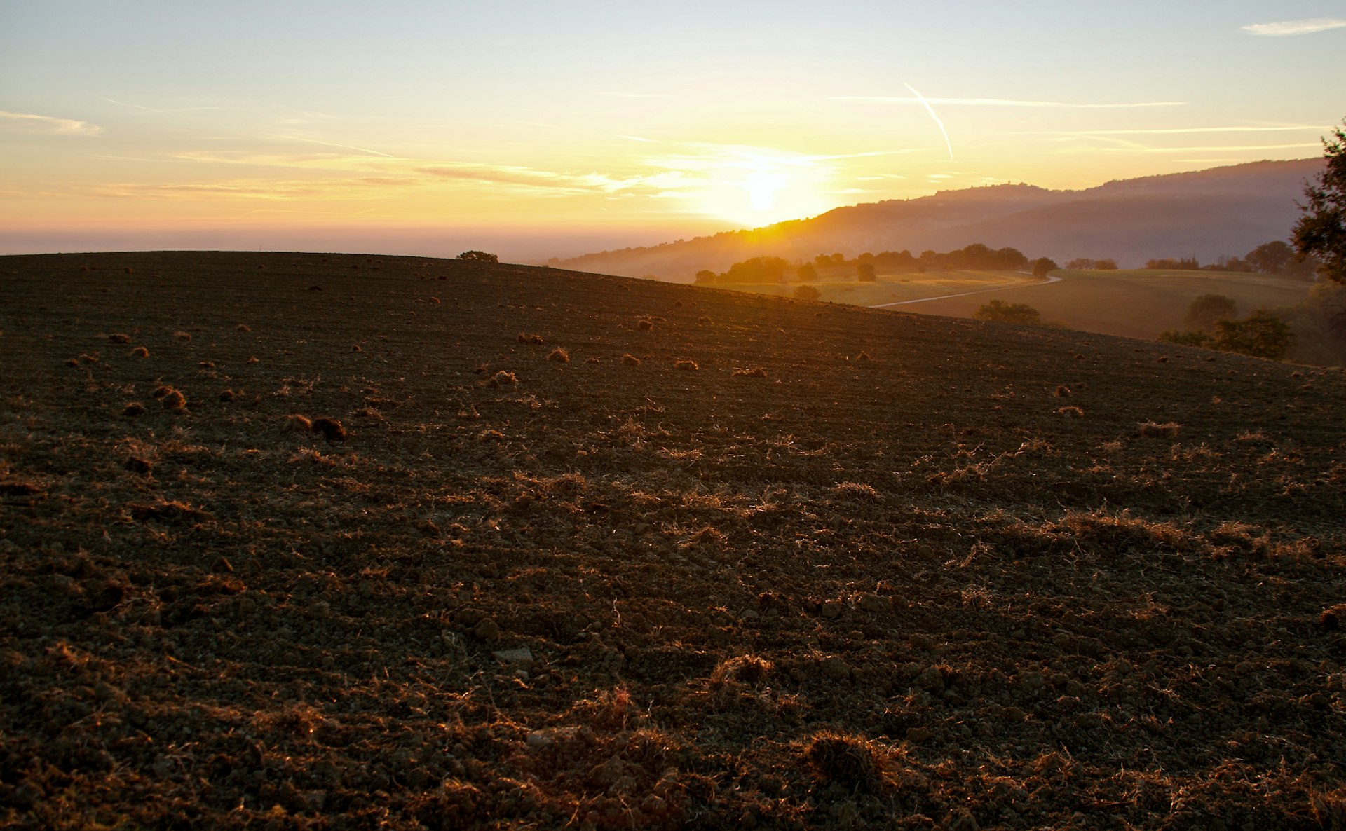 Open land at sunset with warm golden light across dark earth